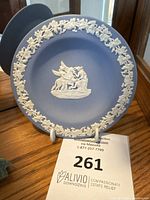 Full view of the blue Jasperware plate with white relief around the rim and central classical design, displayed on a stand.