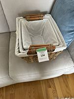 Front and top view of largest wicker basket showing natural woven texture, beige fabric liner with slight dirt marks, and two wooden handles wrapped in wicker.