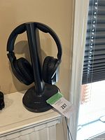 Black Sony wireless over-ear headphones on a black charging stand with power cable shown from two angles.