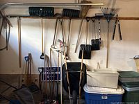 Wide view of yard tools hanging and leaning against the wall showing shovels, rakes, hoe, and broom.