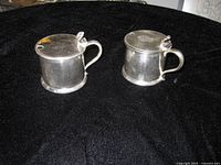 Two matching silver-plate condiment pots with lids closed