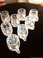 Eight clear handled glass cups displayed on dark surface