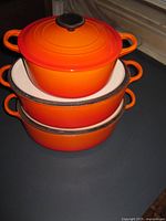 Stacked view of three orange Dutch ovens, showing size gradation and white interiors