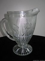 Clear glass footed jug showing handle, spout, floral pattern and pedestal