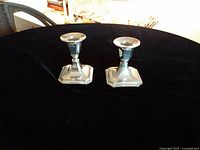Pair of small silver-plated candle holders with square bases on black surface