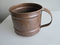 Side view of copper pail showing handle and patina