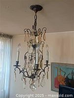 Overall view of chandelier hanging from ceiling showing frame, crystals and bulbs