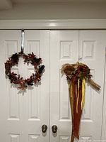 Two autumn themed wreaths hanging on white double doors, showing the full view of both items for sale