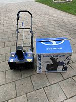 Blue and black SnowJoe snowblower seen from front left angle with its original box next to it.