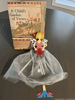 Photo showing book 'A Child's Garden of Verses' and fairy wind chime with fabric skirt and painted wooden figure