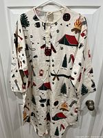 Full front view of the nightshirt hanging on a white hanger, showing camping scene pattern on off-white fabric with button front and long sleeves.
