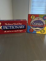 Photo showing the two board game boxes, Cranium and Pictionary, side by side on a table with a window background.