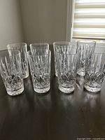 Set of 8 clear crystal highball glasses displayed together on a table, showing uniform cut patterns around the base with no visible damage.
