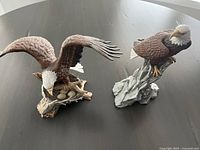 Two ceramic eagle figurines on dark surface, one with open wings over nest with eggs, one perched on rock