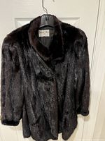 Full view of elegant black mink fur coat hanging, showing overall length and shape.