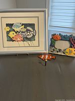 Lot overview showing framed print, fish-themed photo frame, and fish-shaped hook on dark surface