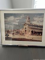 Full view of framed art print showing architectural scene with people, carriages, and a clock tower building under a cloudy sky.