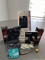 Photo showing golf balls, black leather glove in box, socks, golf tees, ball marker set, and metal golf bookmark