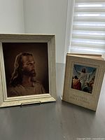 Wooden framed portrait of Jesus and hardback book 'Beautiful Bible Stories' standing on table.