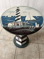 Top-down view of round tabletop showing a lighthouse and sailboats painted on surface with crackled finish.