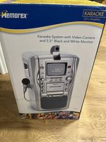 Photo of the Memorex karaoke system box showing the product image with integrated 5.5-inch black and white monitor and video camera on top.