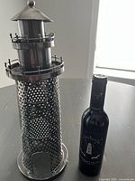 Metal lighthouse wine bottle holder standing upright next to a wine bottle for scale.