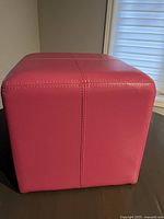 Side view of the pink faux leather ottoman showing vertical and horizontal stitched seams.