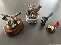 All four ceramic bird figurines displayed together on a flat surface showing variety of sizes and colors.