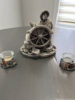 Resin sailor statue holding ship's wheel with two seaside votive holders on either side