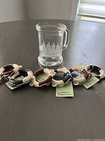 Photo showing one clear glass stein with etched sailboat drawing and six nautical-themed napkin rings in burgundy, navy, and cream colors.