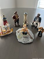 All nautical resin figurines arranged on a dark surface including lighthouses, pirate, sailors, fisherman, and boat.