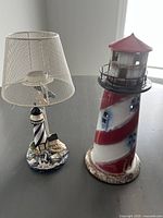 Photo showing both nautical themed lights on a table: the lamp with mesh shade and the ceramic lighthouse tealight holder.