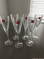 Set of six clear RCR Cristaleria Italiana champagne flute glasses, each with red RCR sticker visible, standing on a dark surface.