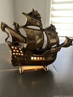 Front view showing the solid brass sailing ship lamp illuminated from inside with visible window cutouts and detailed sails.