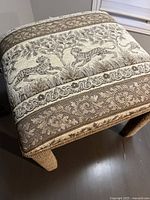 Close-up of foot stool top showing leopard motif and floral pattern tapestry fabric upholstery in beige and brown.