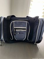 Front view of Exess travel bag showing front pocket with logo, shoulder straps, and zippered compartments.