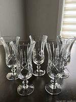 Wide shot showing all five etched crystal parfait glasses arranged on a table, highlighting their flared rims, etched vertical and cross-hatched detailing, and round bases with stems.