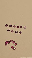 Multiple pear-shaped ruby gemstones arranged on a beige background showing clarity and color variations under neutral light.