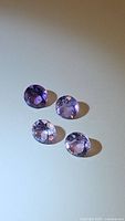 Four faceted natural amethyst gemstones displaying a light to medium purple color laid out on a plain surface.