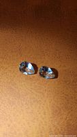 Pair of pear cut natural aquamarine gemstones on a brown background, showing light blue color and good clarity.