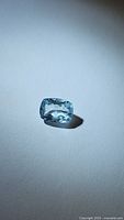 Single natural aquamarine cushion cut gemstone photographed on a plain light background showing facets and clarity details.