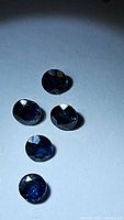Five loose round cut blue sapphires arranged on white background under direct light to show cut and color.