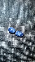 Two natural blue star sapphire oval cabochons on textured surface, showing prominent six-ray star effect on each stone.