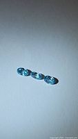 Three natural oval cut blue zircon gemstones shown together on white background under bright light to highlight color and clarity.