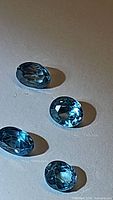 Four oval-cut seafood blue natural Cambodian zircon gemstones laid out on a neutral background, showing facets and reflections.