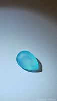 Photo of a single pear-shaped deep icy blue chalcedony gemstone with smooth polished surface on a white background.