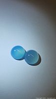 Close-up photograph of two natural blue chalcedony cabochon gemstones placed side by side on white background, showing color, shape and size.