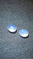Two natural oval cabochon chalcedony stones displayed on textured black surface, showing smooth polished translucent blue appearance.