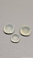 Three tea green chalcedony gemstones arranged on a light surface, showing faceted checkerboard cuts and translucent quality.