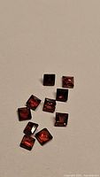 Photo showing ten natural garnet gemstones with princess cut, arranged loosely on a flat surface.